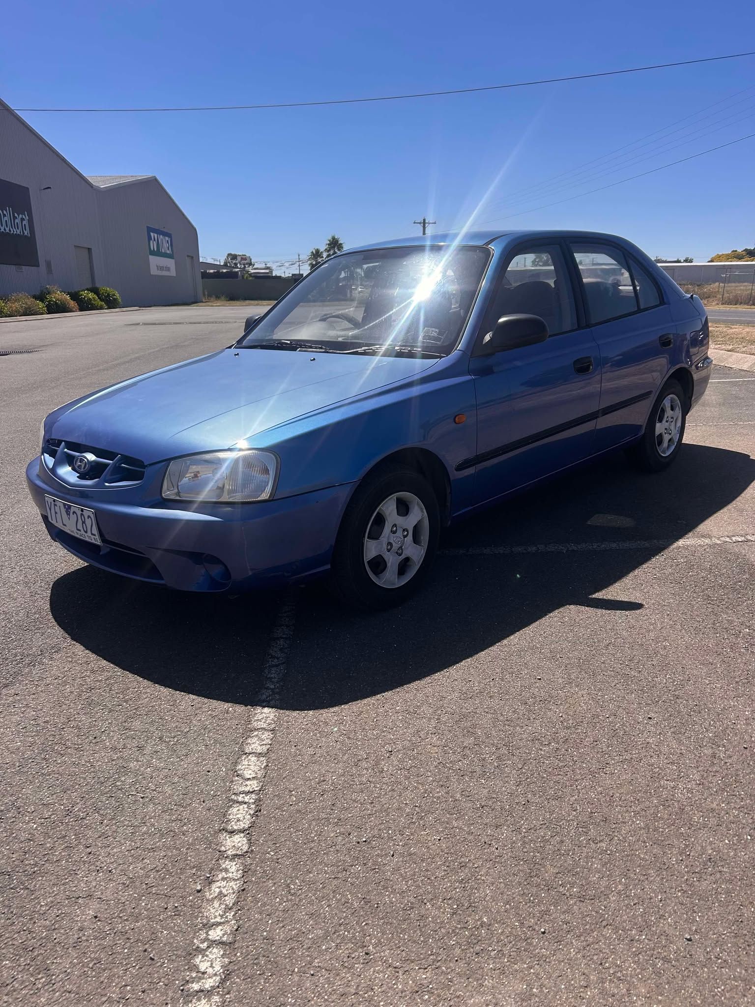 A blue car is parked in a parking lot in front of a building.