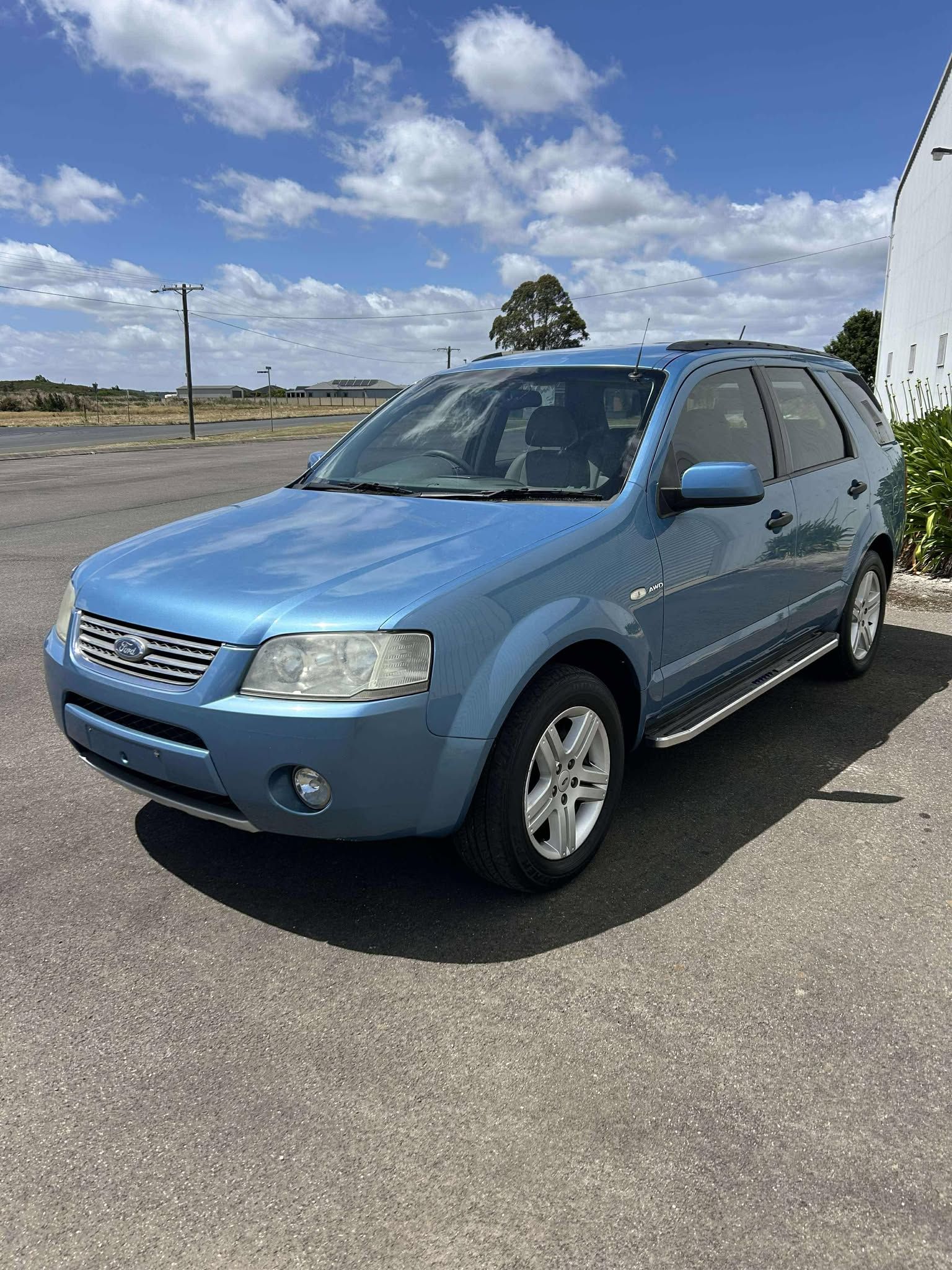 A blue ford escape is parked in a parking lot.