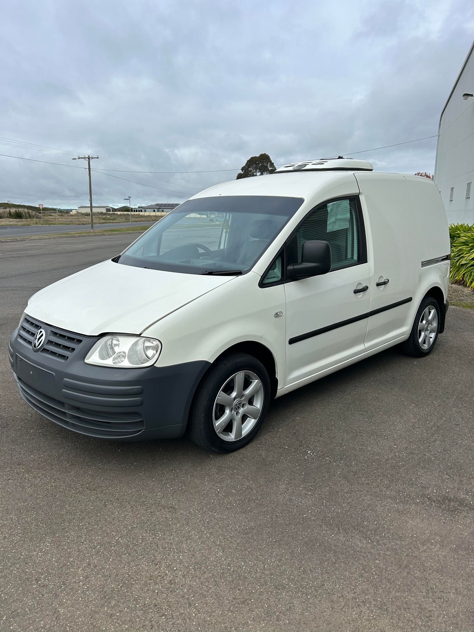 A white volkswagen is parked in a parking lot in front of a building.