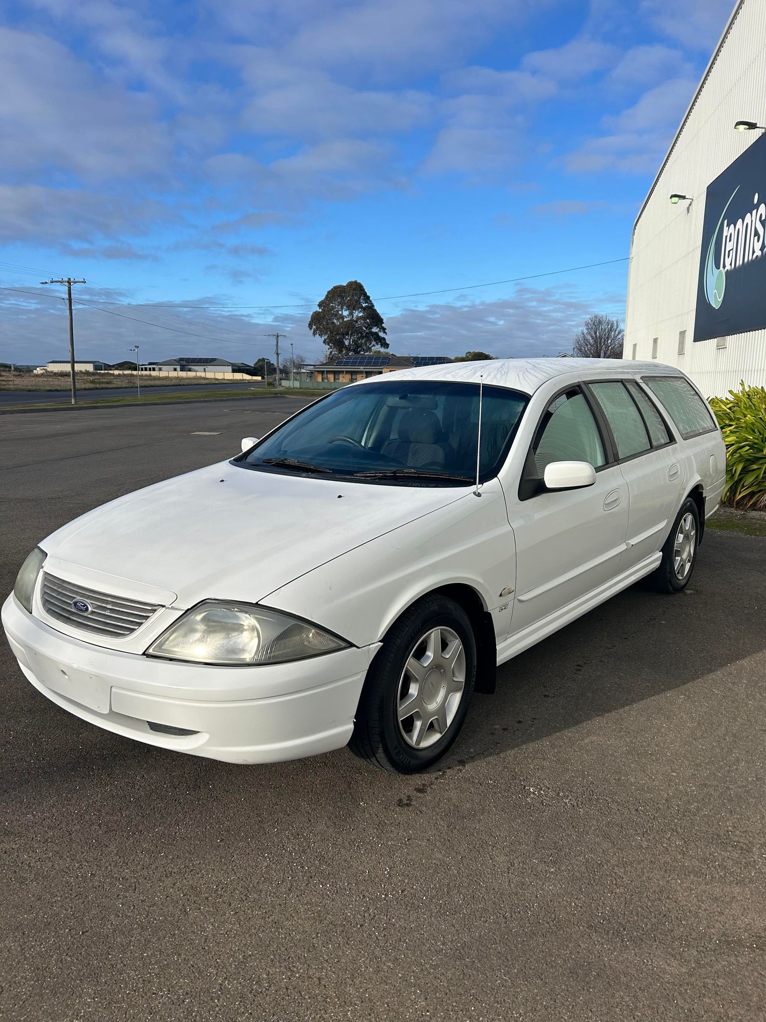 A white station wagon is parked in a parking lot in front of a building.