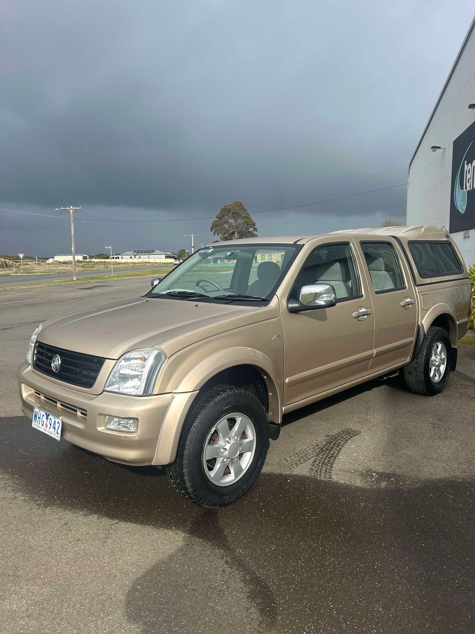 A gold truck is parked in a parking lot in front of a building.