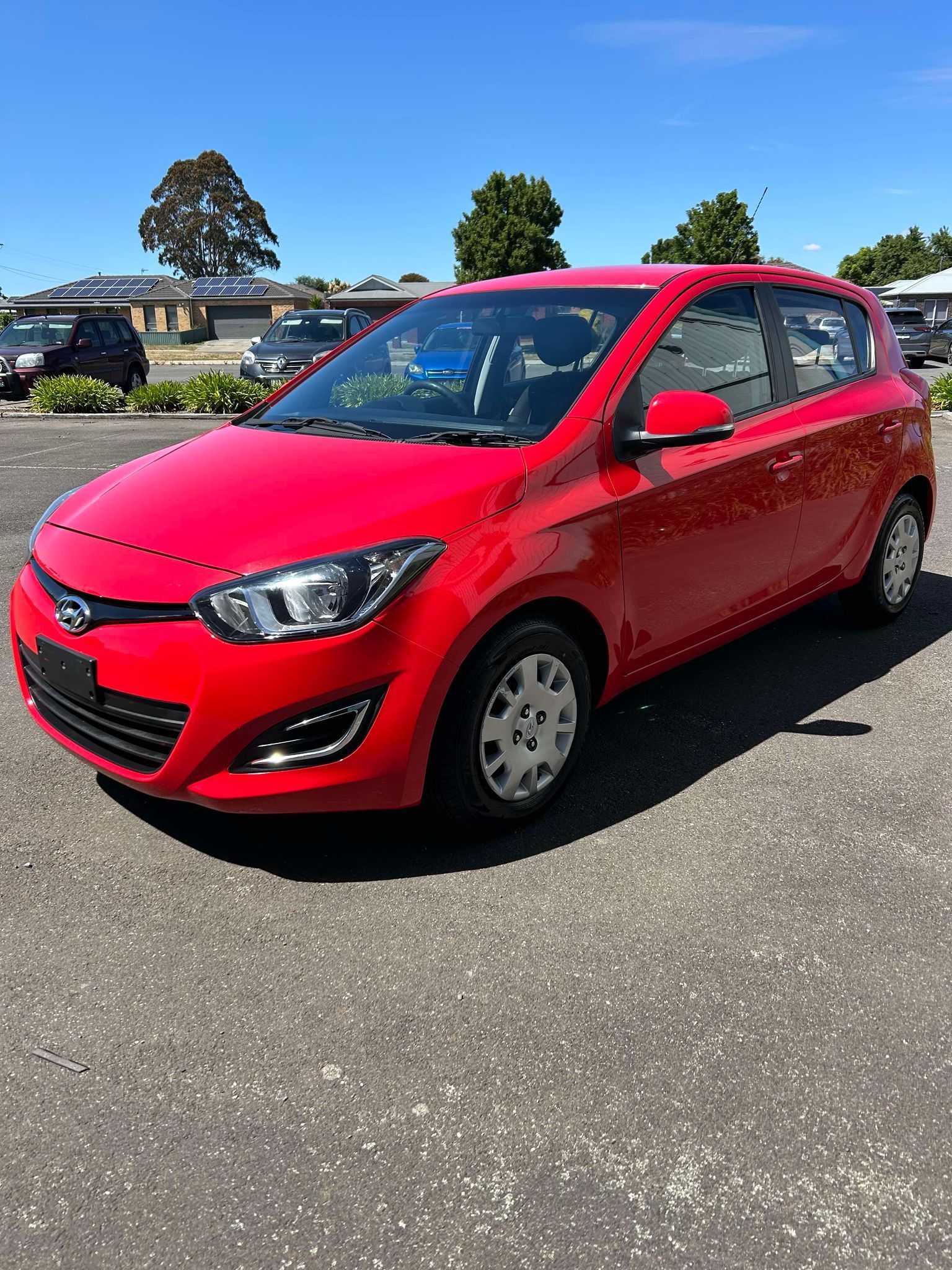 A red car is parked in a parking lot on a sunny day.