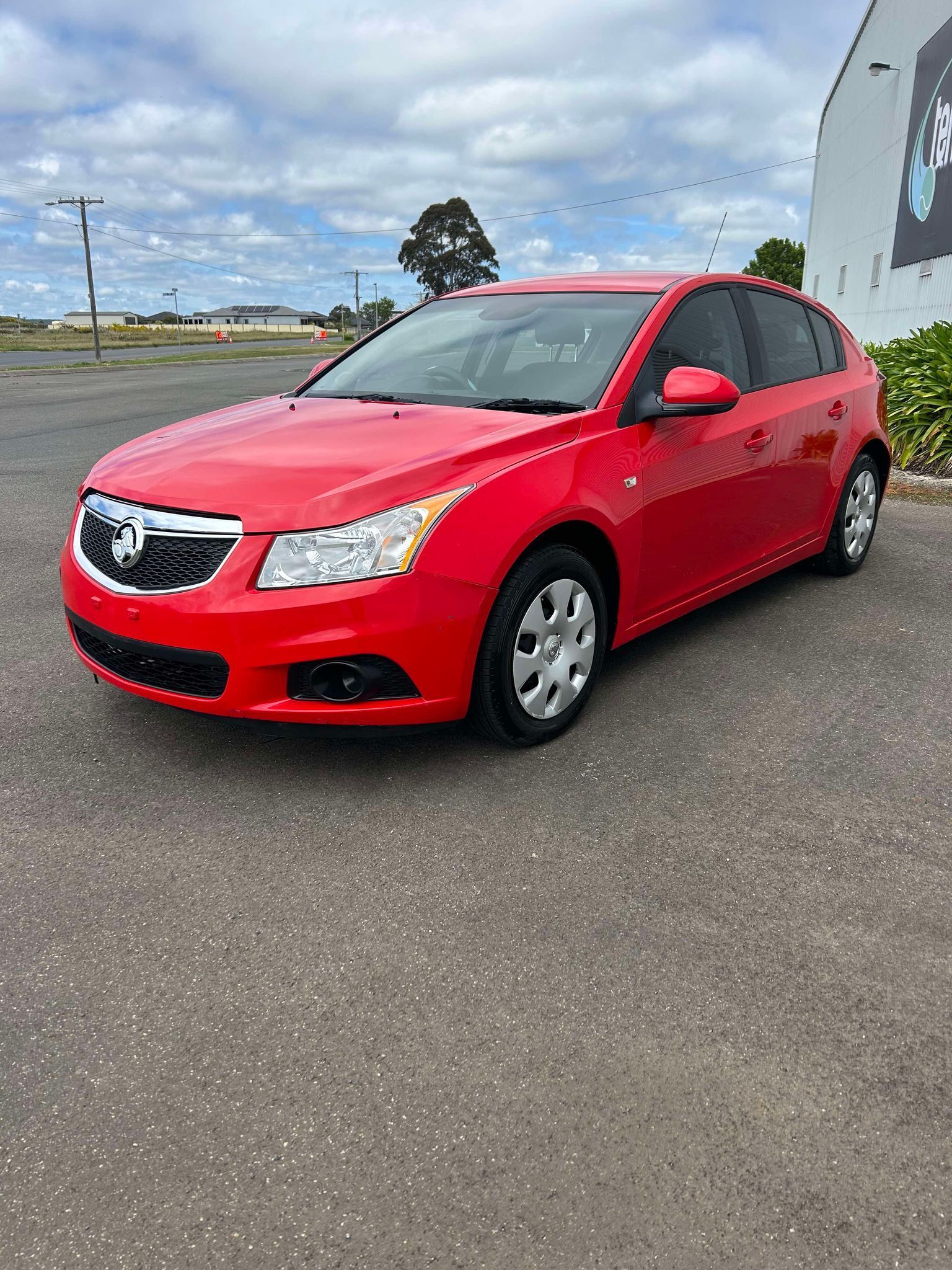 A red car is parked in a parking lot in front of a building.