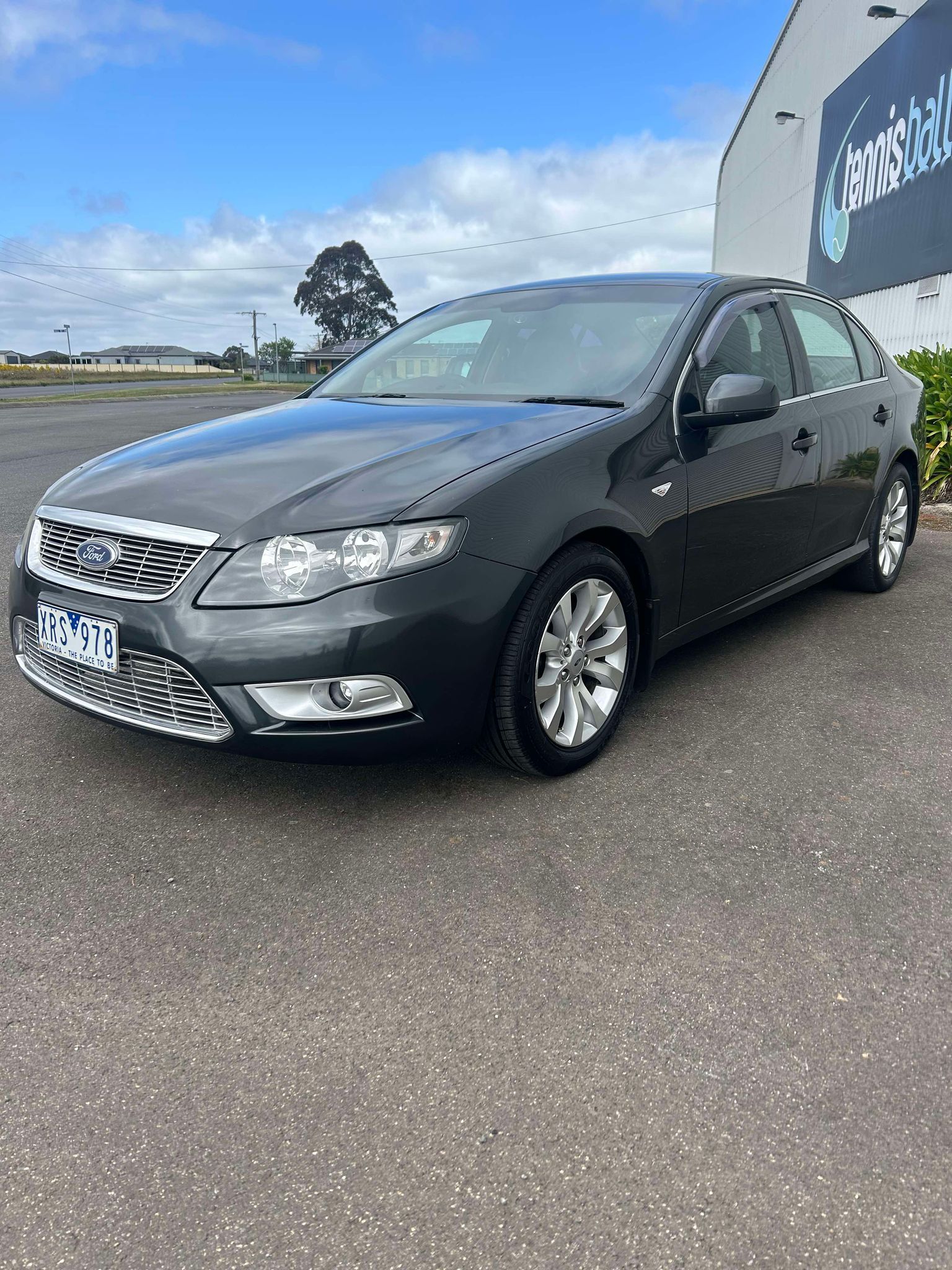 A black car is parked in a parking lot in front of a building.