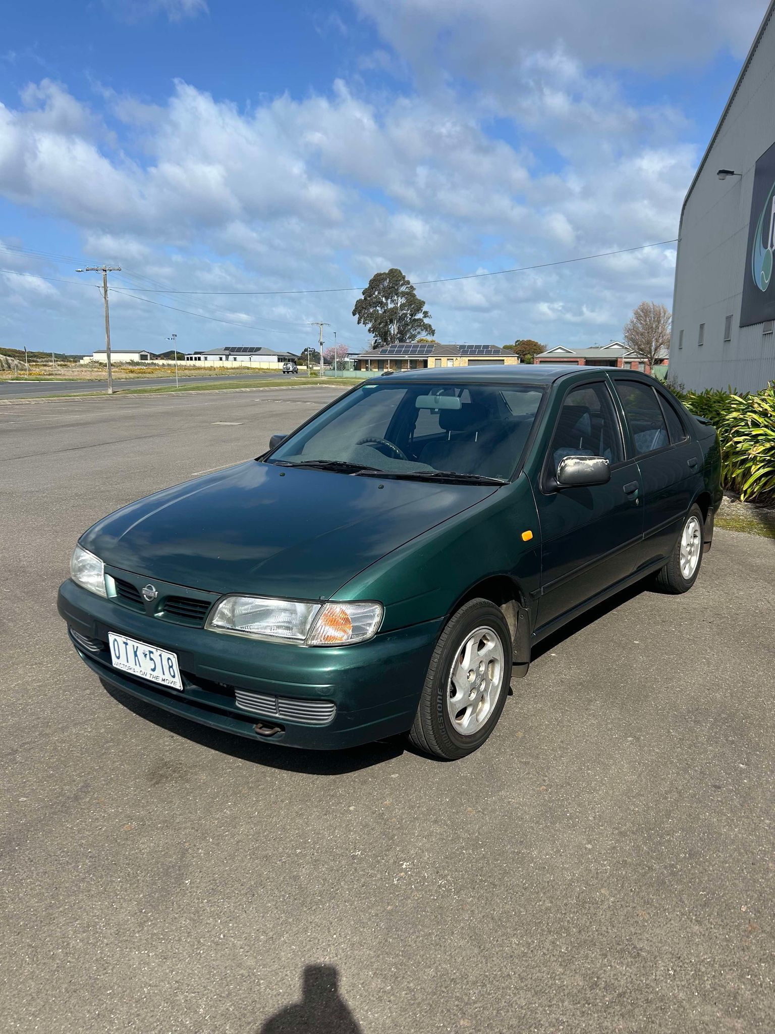 A green car is parked in a parking lot in front of a building.