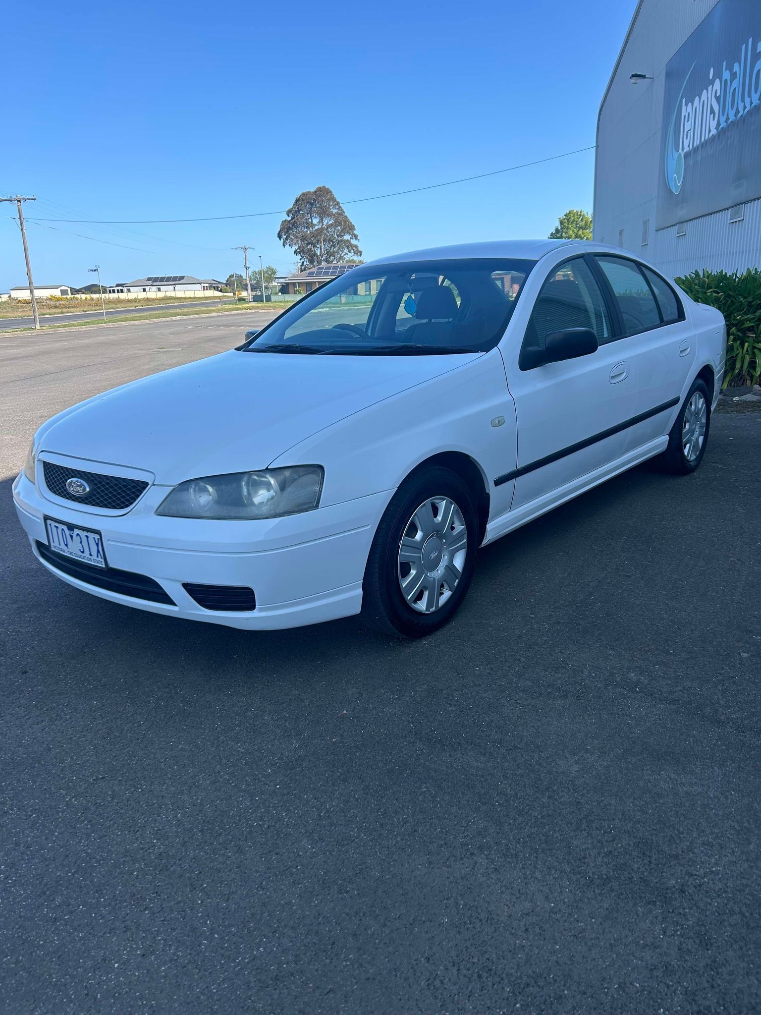 A white car is parked in a parking lot in front of a building.