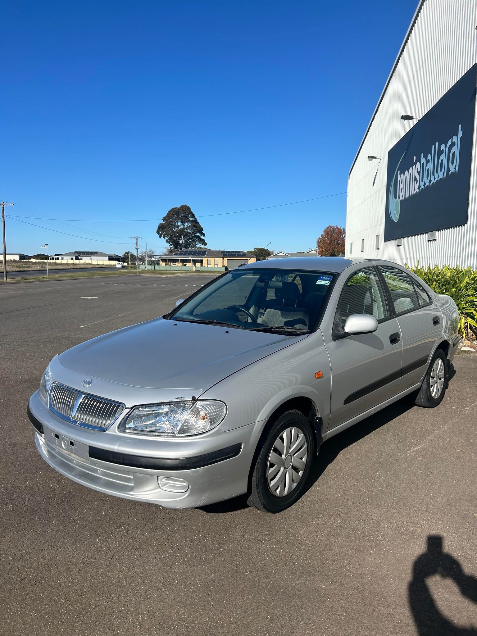 A silver nissan is parked in a parking lot in front of a building.