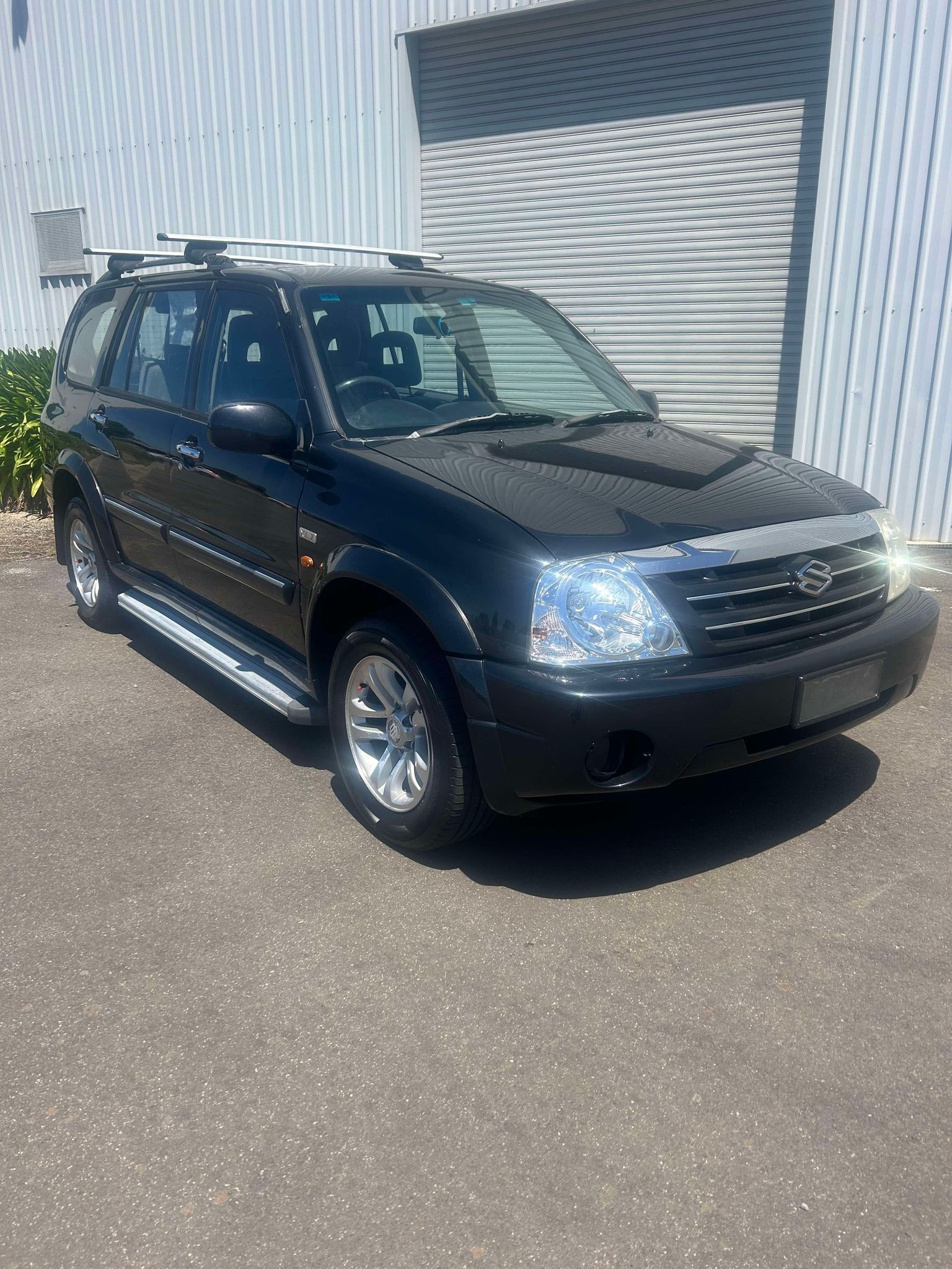 A black suv with a surfboard on the roof is parked in front of a building.