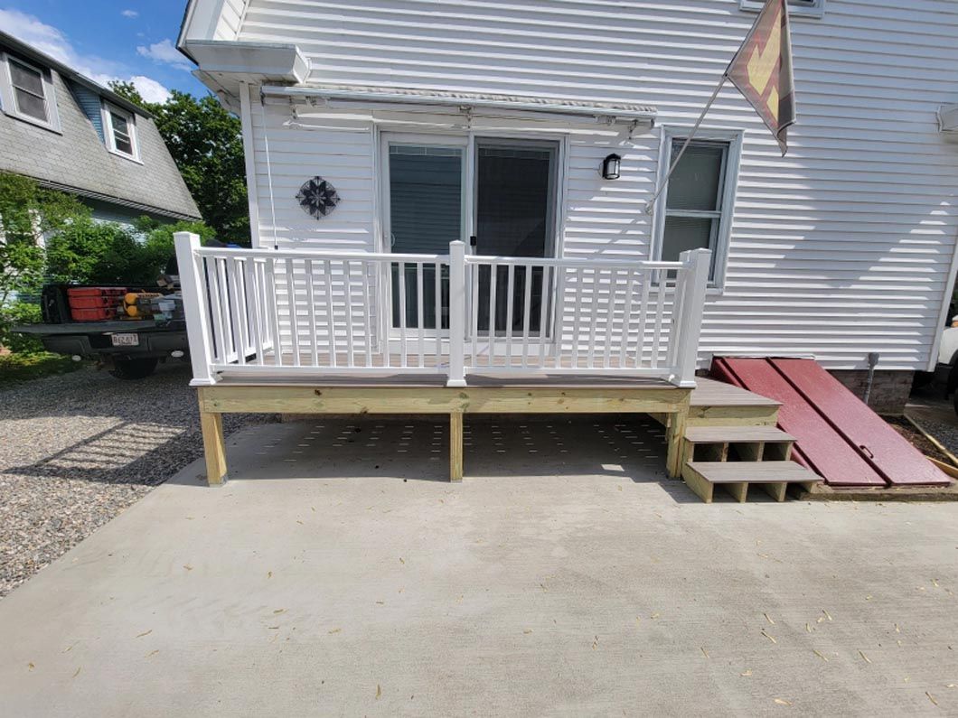 A white house with a wooden deck and stairs in front of it.