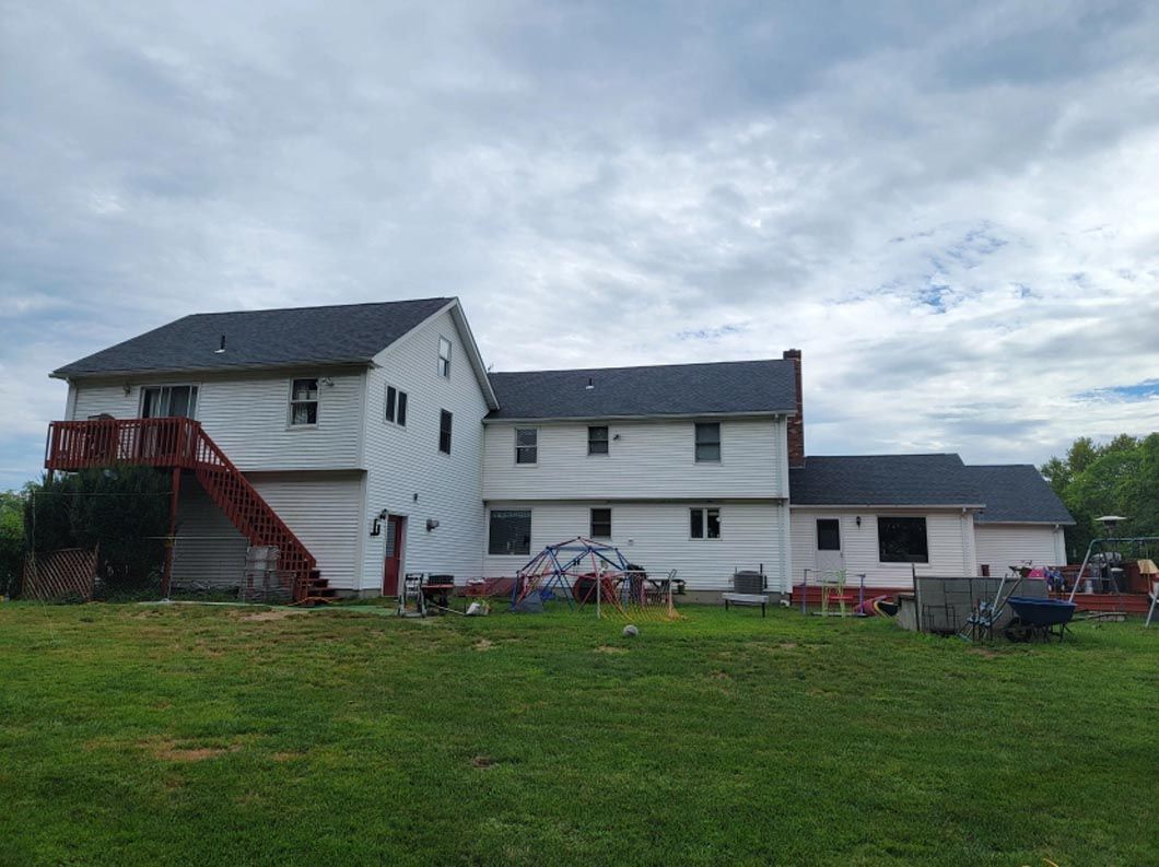 A large white house with a black roof is sitting on top of a lush green field.