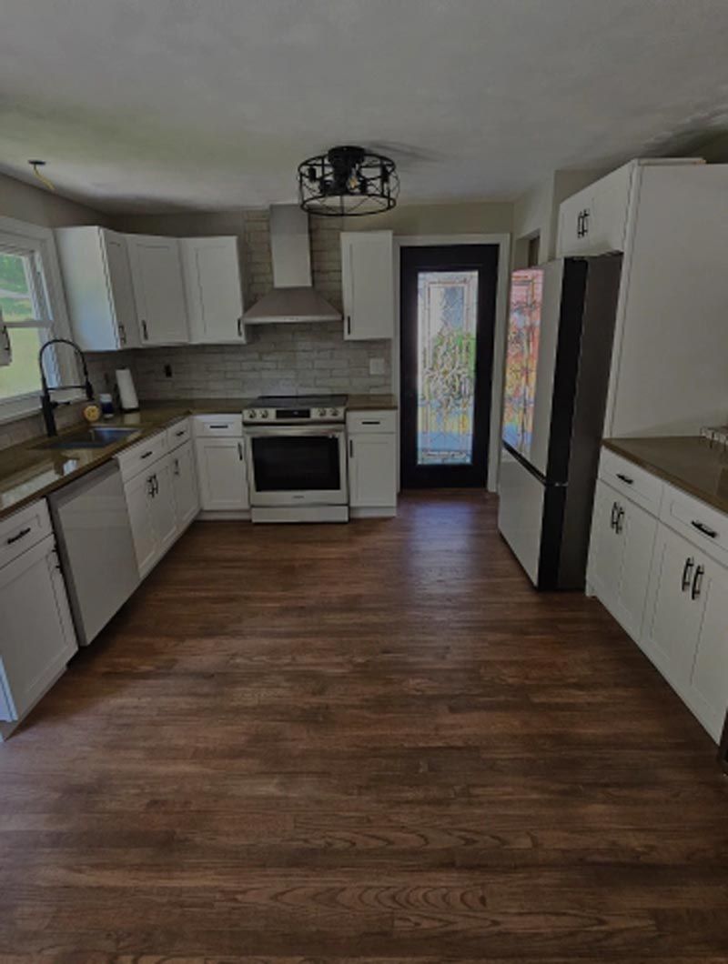 A kitchen with hardwood floors , white cabinets , a stove , a refrigerator , and a sink.