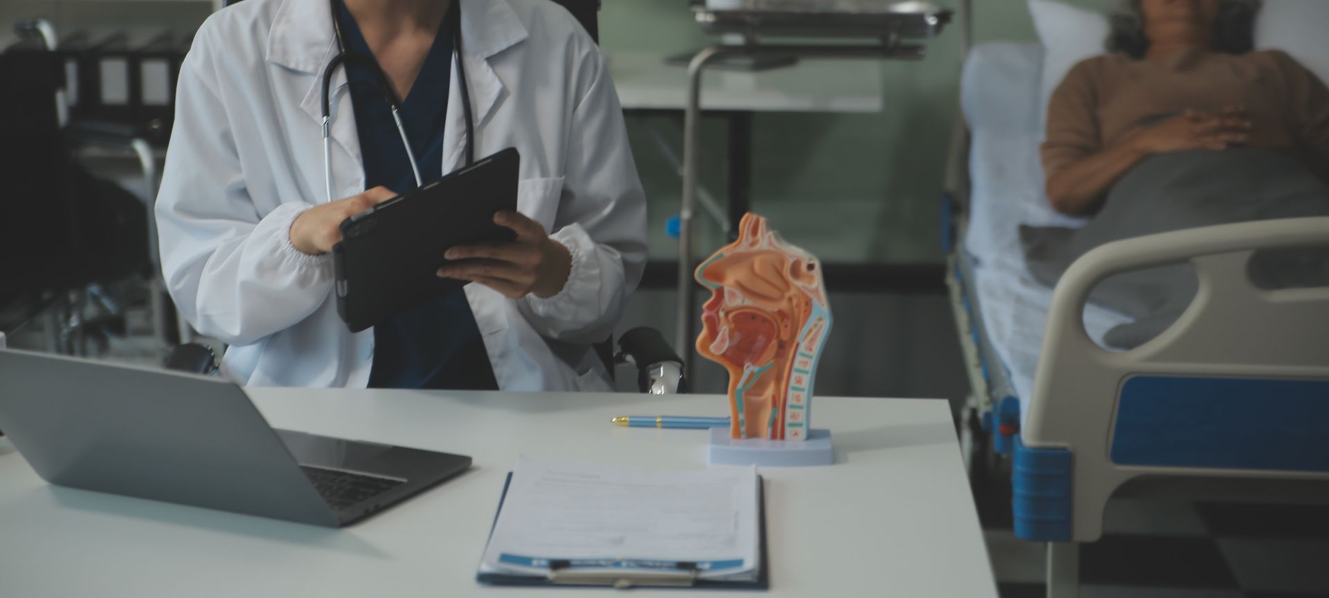 Doctor with tablet and anatomy model in a hospital room, patient in bed.
