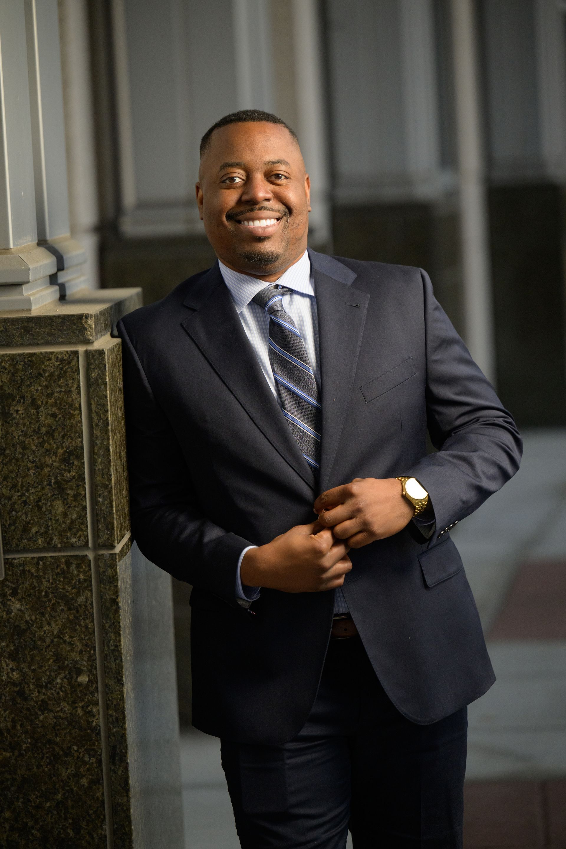 Man in a suit and red tie, smiling; library background.