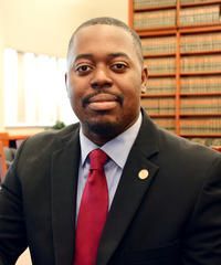 Man in a suit and red tie, smiling in a library.