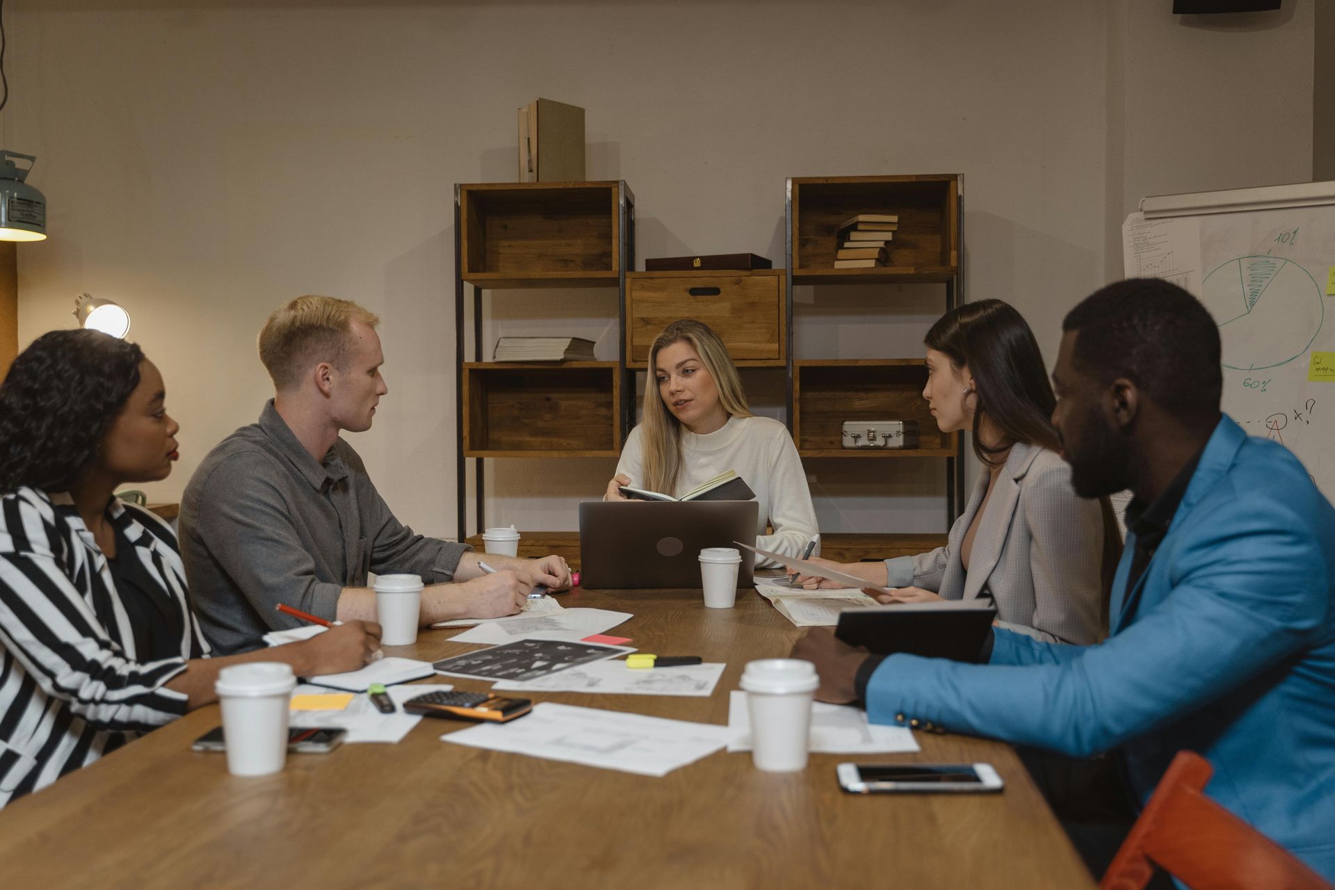 A diverse group of people in a meeting, gathered around a table with a laptop and papers.