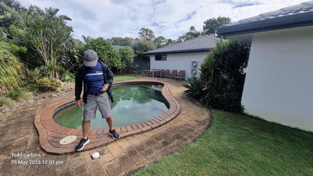 Person stands near a kidney-shaped pool. Trees and house are in the background, blue sky overhead.