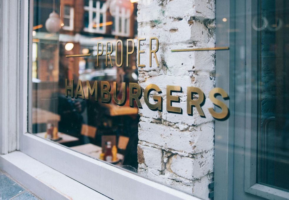 A restaurant window with a sign that says `` proper hamburgers '' on it.
