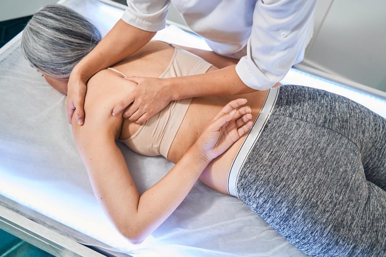 Donna che riceve un massaggio alle spalle, sdraiata su un lettino, con le mani del terapeuta sulla schiena.