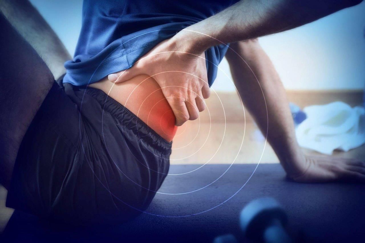 Persona in abbigliamento sportivo che si tiene l'anca, a indicare dolore. La luce rossa evidenzia la zona dell'anca, a indicare una lesione.