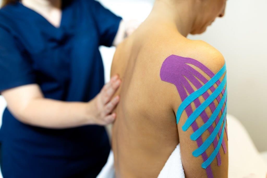 Persona con nastro kinesiologico viola e blu sulla spalla sottoposta a fisioterapia.