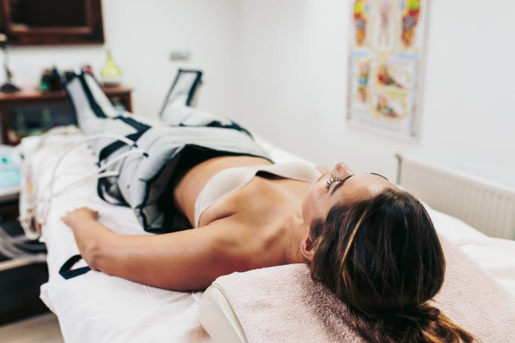 Donna sottoposta a trattamento di drenaggio linfatico, sdraiata su un letto con dispositivi di compressione alle gambe.