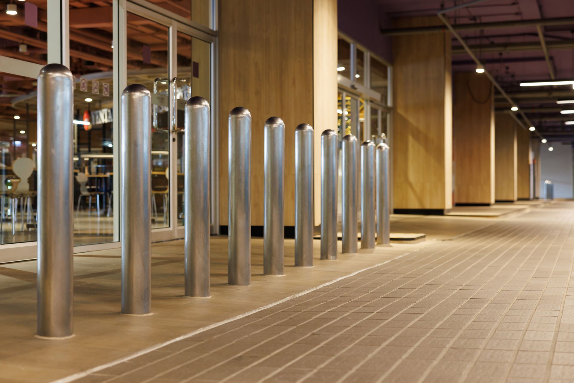 A row of stainless steel poles are lined up on a sidewalk in front of a building.
