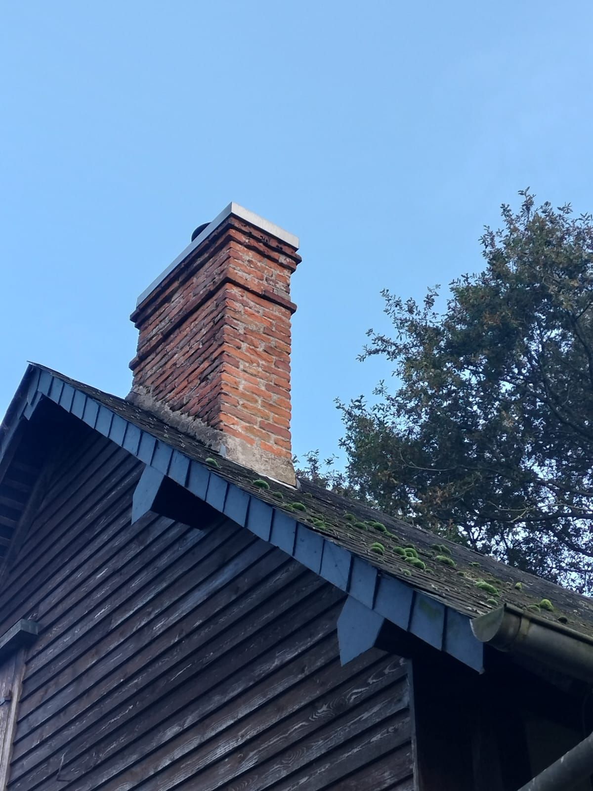 Cheminée en briques sur une maison en bois au toit sombre, avec un ciel bleu en arrière-plan.