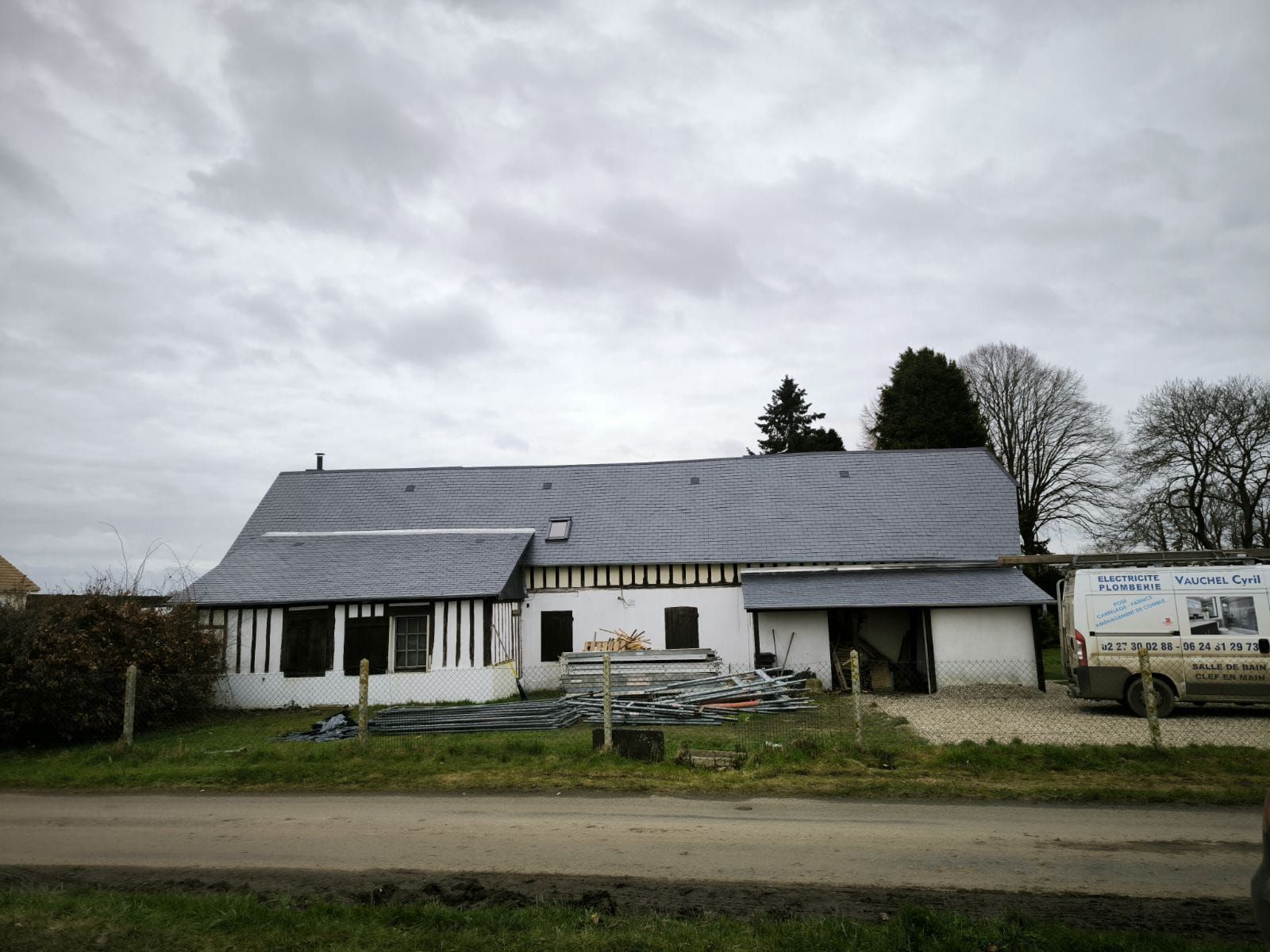 Un bâtiment de deux étages au toit sombre et aux murs blancs, sous un ciel nuageux.