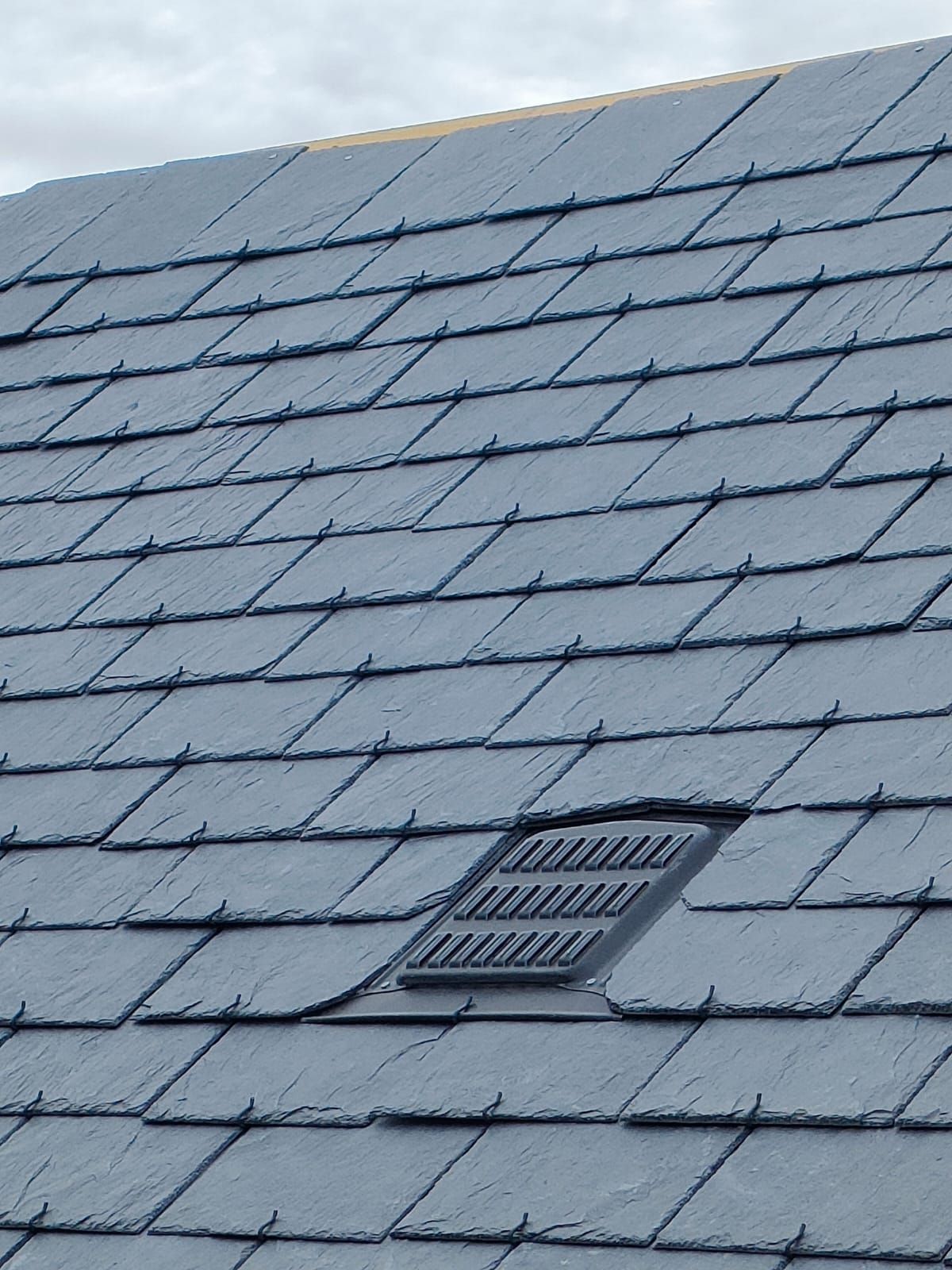 Toit en ardoise gris foncé avec une grille d'aération rectangulaire.