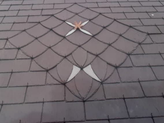 Toiture en ardoise ornée d'un motif décoratif en losanges rehaussé de touches de blanc.