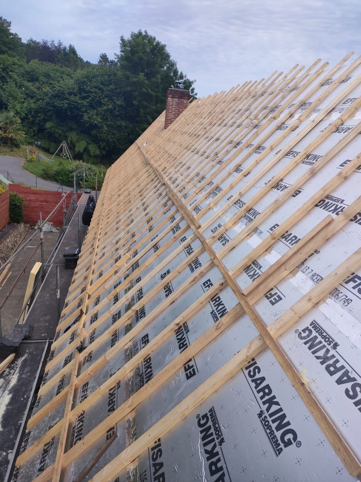 Toiture en construction : charpente en bois et isolation sur un toit en pente.