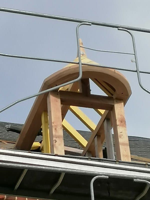 Charpente en bois d'une toiture incurvée en construction. Échafaudages visibles.