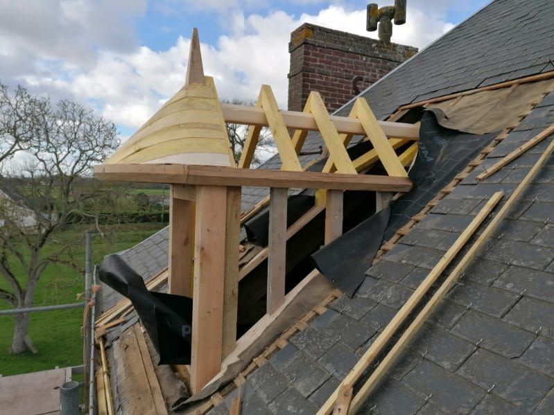 Construction de toiture avec ossature bois, lucarne inachevée et ancienne toiture en ardoise partiellement enlevée.