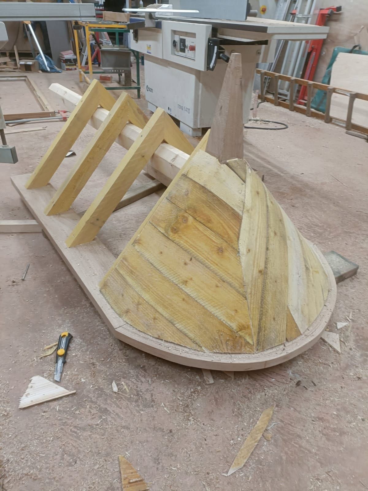 Sculpture en bois en cours de réalisation ; base en bois clair, façade à chevrons, supports inclinés, décor d'atelier.