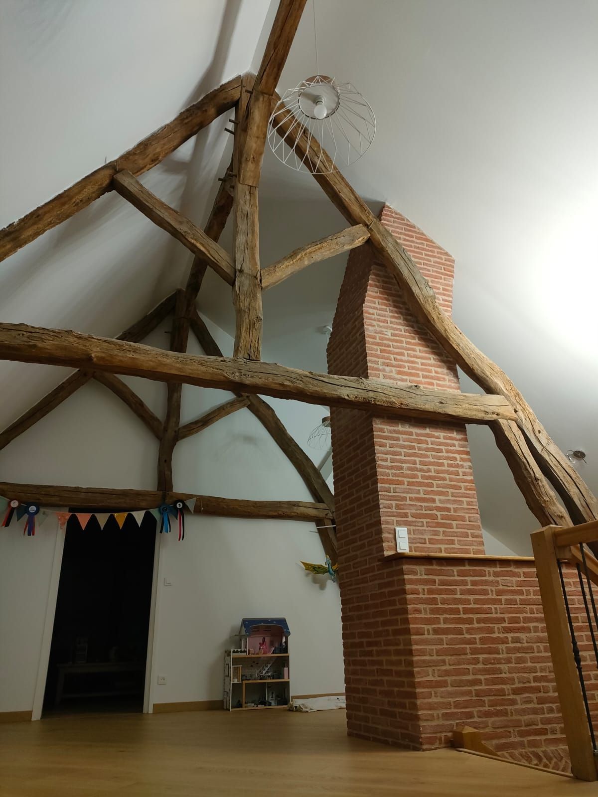 Poutres en bois dans une pièce aux murs blancs avec une cheminée en briques et une porte ouverte.