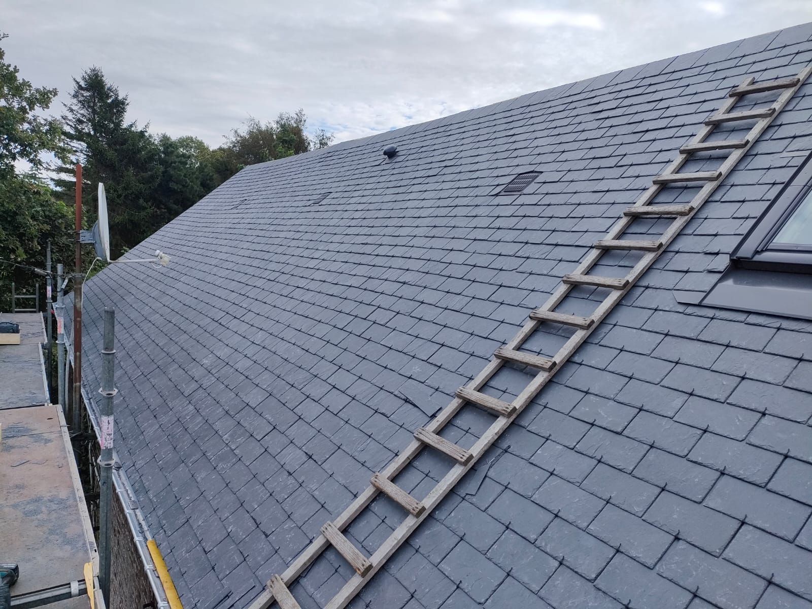 Toit en ardoise avec échelle en bois, ciel nuageux.