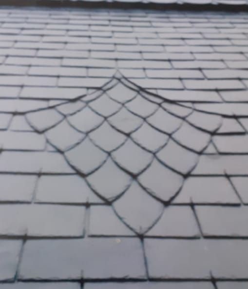 Gros plan sur un toit d'ardoise orné d'un motif décoratif en losange composé de tuiles en écailles de poisson.