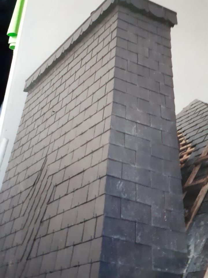 Cheminée recouverte d'ardoises sur un toit, ardoises gris foncé disposées en rangées décalées.