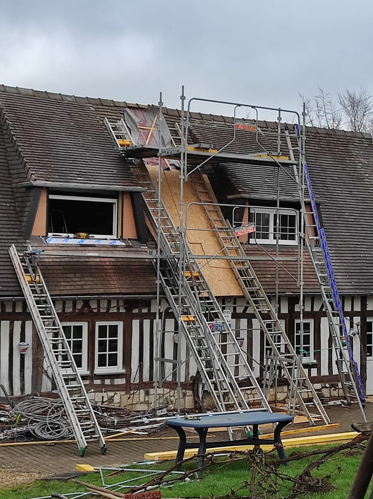 Échafaudages et échelles adossés à une maison à colombages pour des travaux de réparation de toiture. 