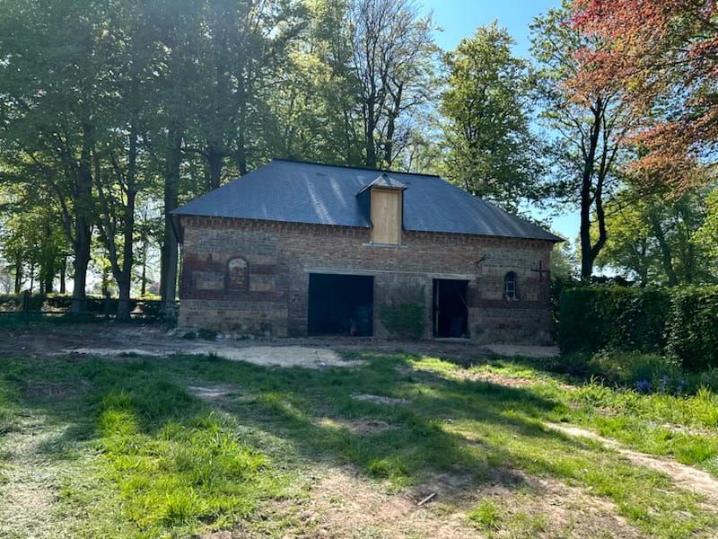Bâtiment en briques au toit sombre, aux portes ouvertes et aux petites fenêtres cintrées,