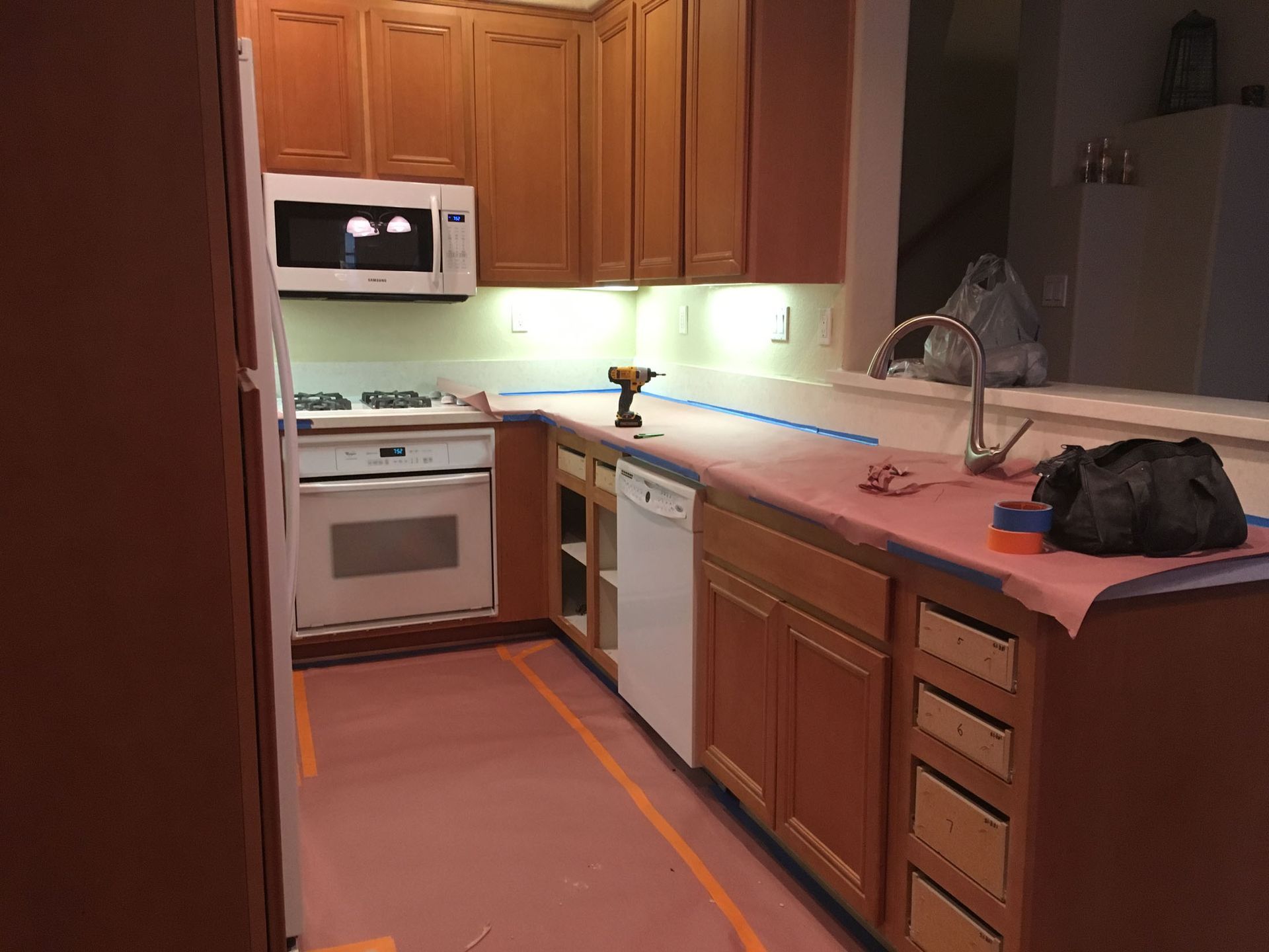 Kitchen with cabinets, microwave, oven, dishwasher, and sink. Countertops have a red protective cover.