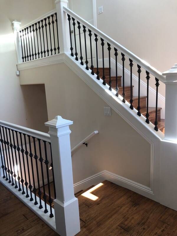 Staircase with white railing and black spindles, wooden steps, and a light-colored wall.