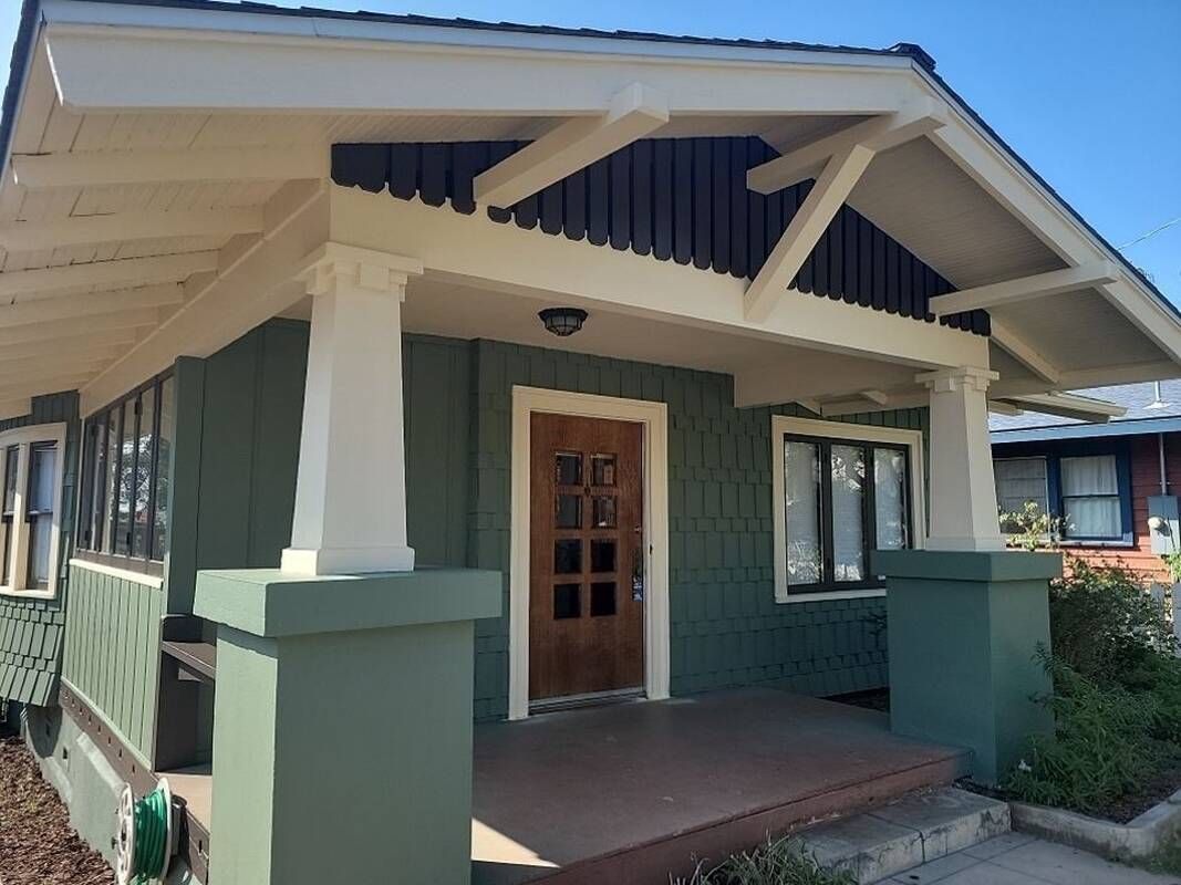Green Craftsman house with white pillars and dark brown door.