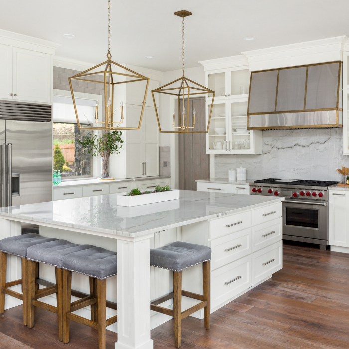 White kitchen with marble island, gold pendant lights, stainless steel appliances, and wood floors.