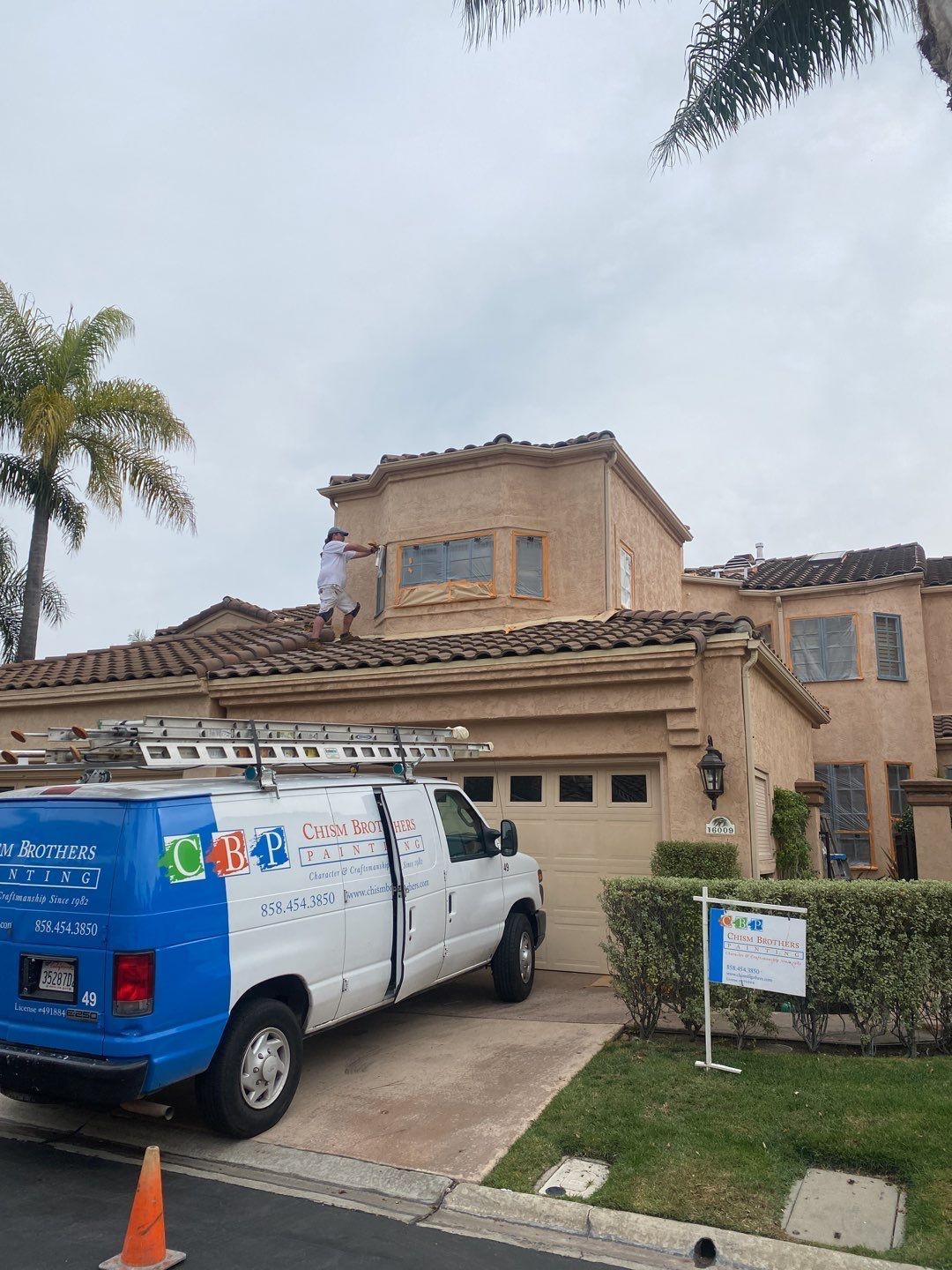 A roofing crew working on a two-story beige house with a TRC truck parked in the driveway.