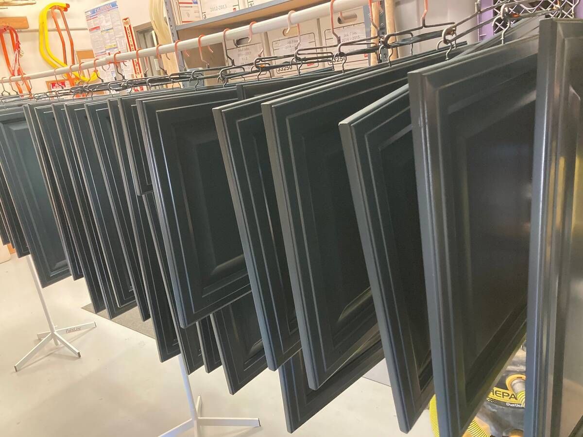 Painted dark gray door panels hanging on a rack. Workshop setting.