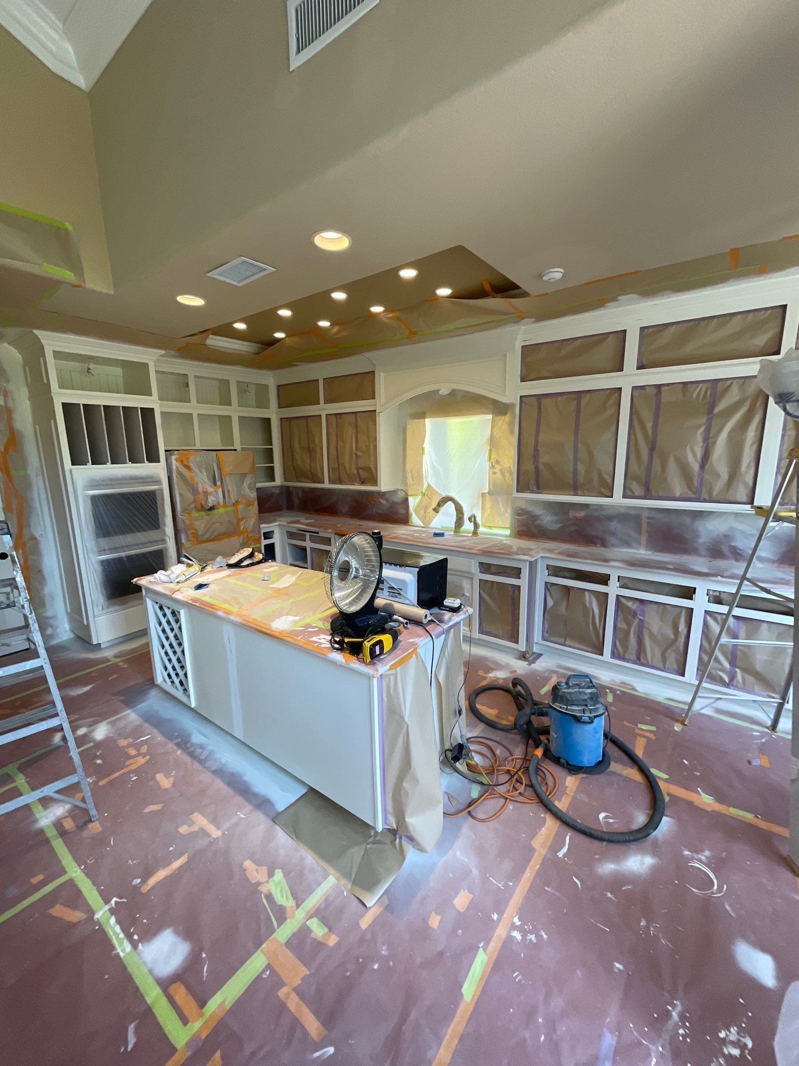 Kitchen remodel: cabinets and island prepped for painting; drop cloths on the floor; ladder present.