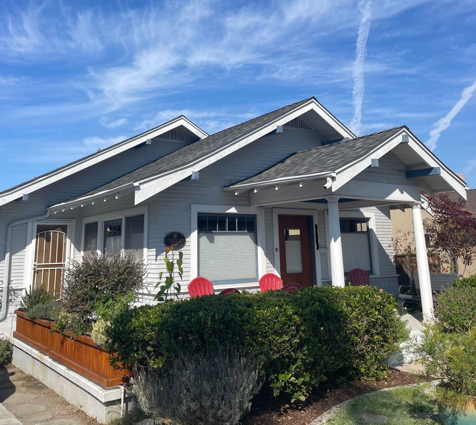 A light blue Craftsman home with a porch, plants, and a bright blue sky.