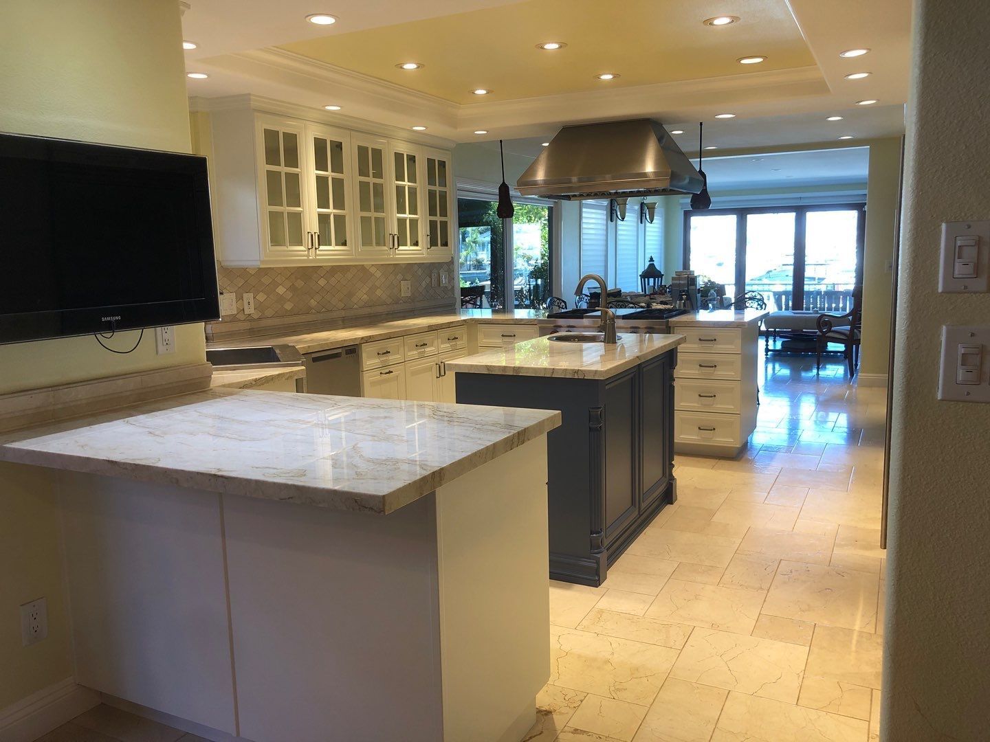 Spacious kitchen with marble countertops, two islands, stainless steel range hood, and a view of an outdoor dining area.