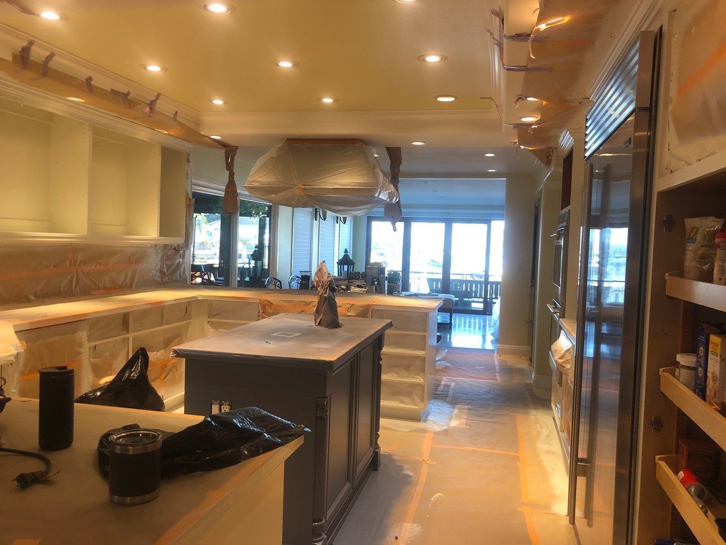 Kitchen under renovation; island, cabinets, appliances covered in protective materials, bright interior with natural light.